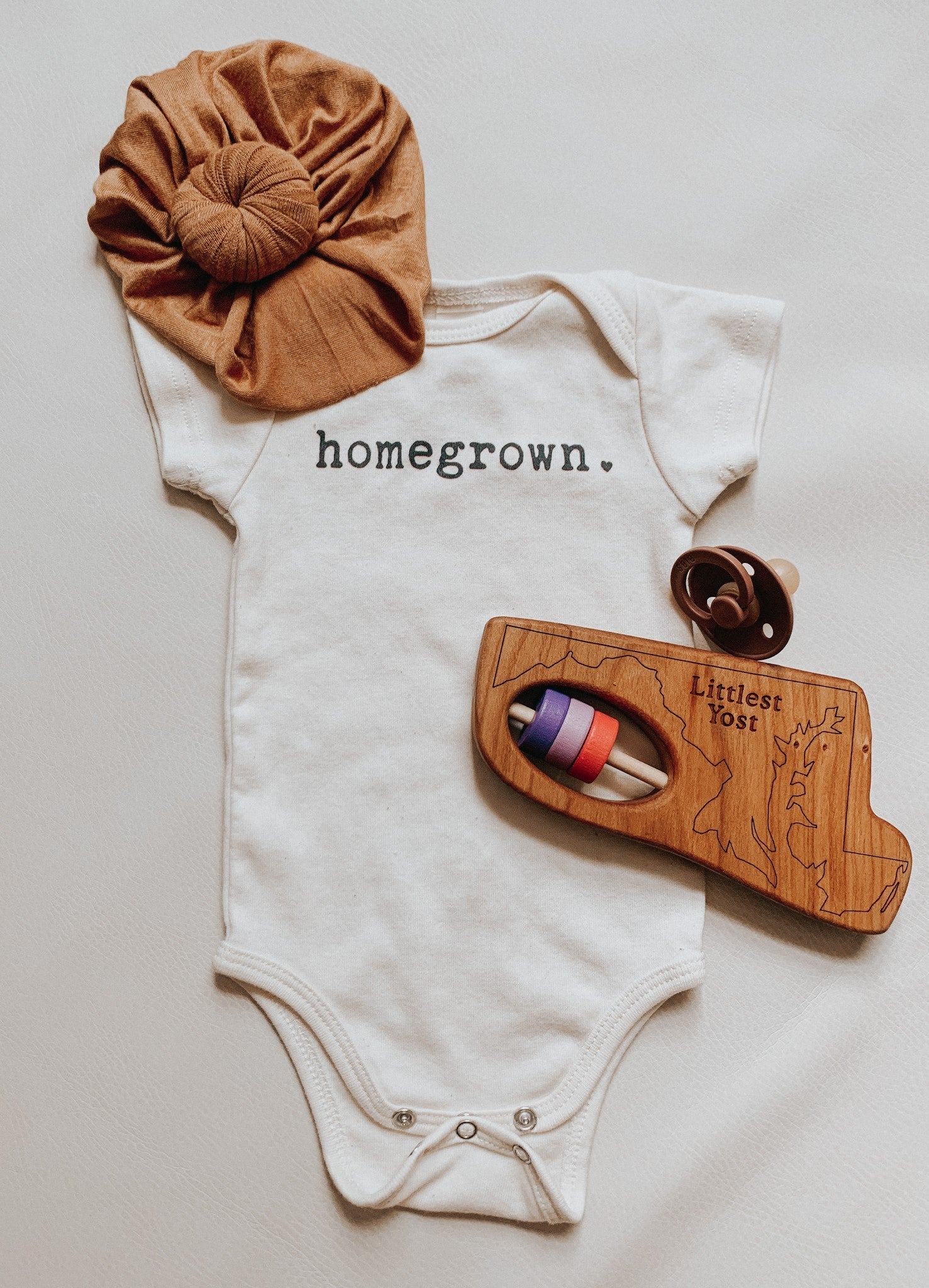 Maryland State Wooden Baby Rattle™  next to a onesie - Bannor-toys
